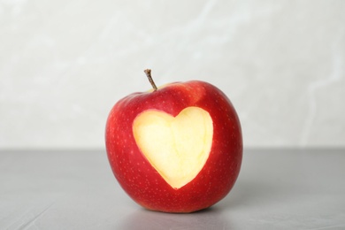 Red apple with carved heart on table against light background