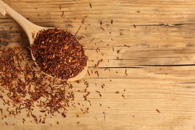 Photo of Spoon with dry rooibos leaves on wooden table, flat lay. Space for text