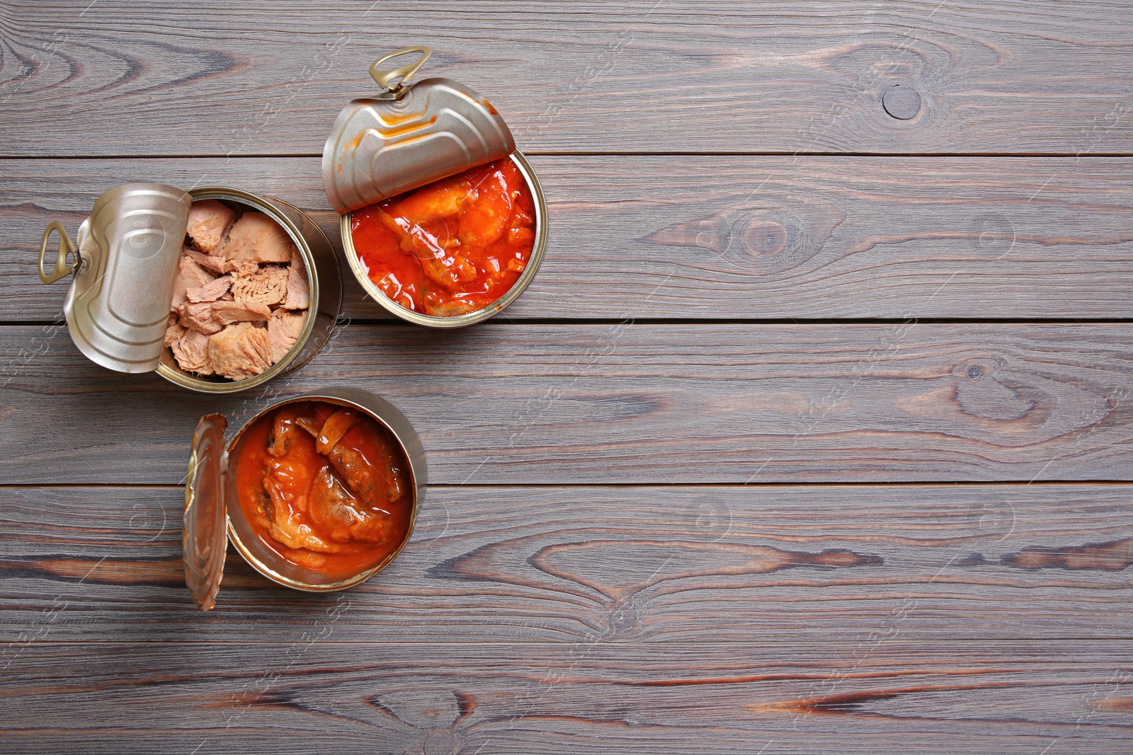 Photo of Tin cans with fish on wooden table, flat lay. Space for text