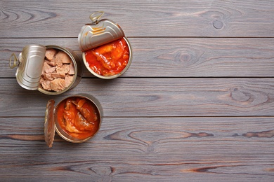 Tin cans with fish on wooden table, flat lay. Space for text