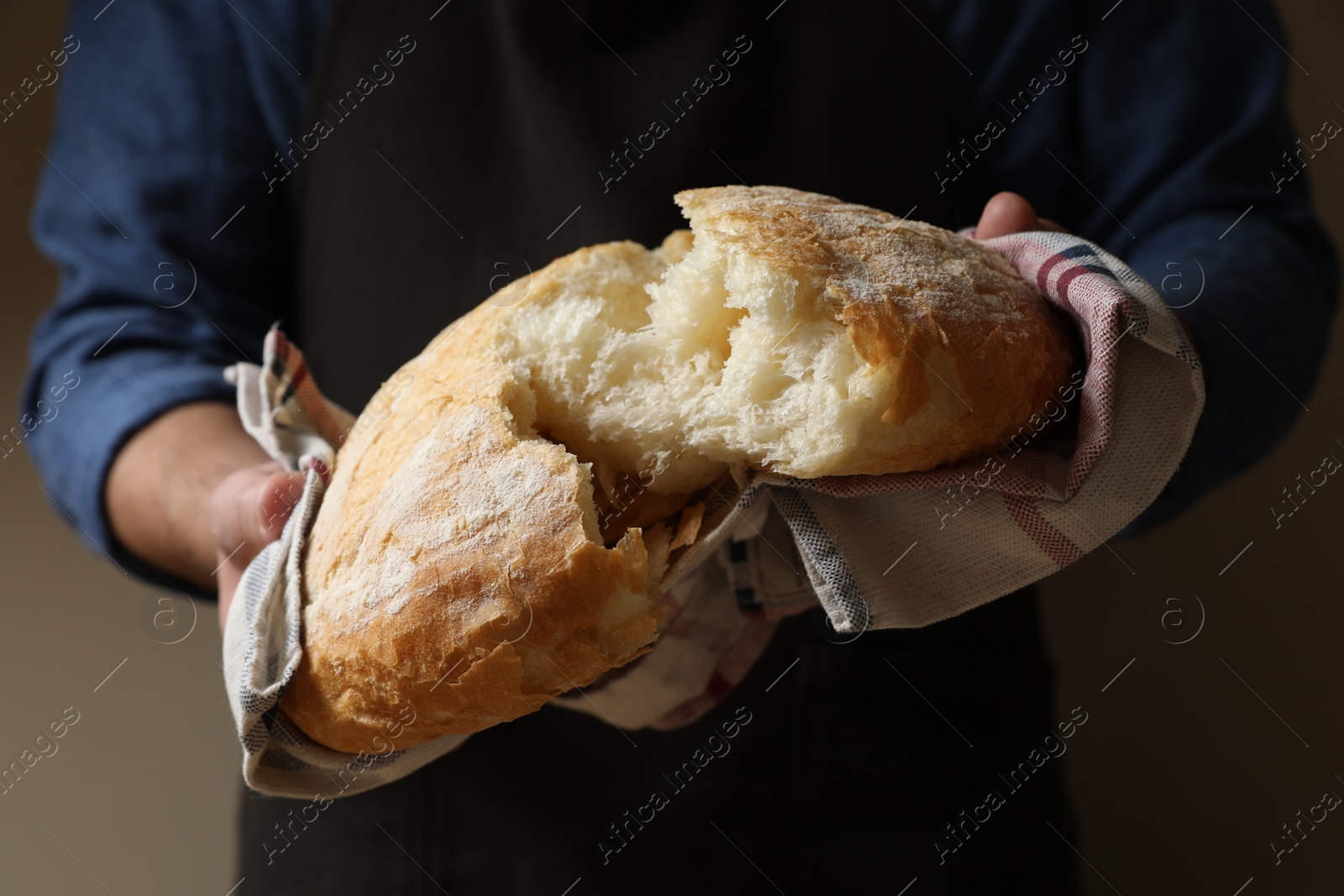 Photo of Man breaking loaf of fresh bread on dark background, closeup