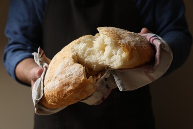 Photo of Man breaking loaf of fresh bread on dark background, closeup