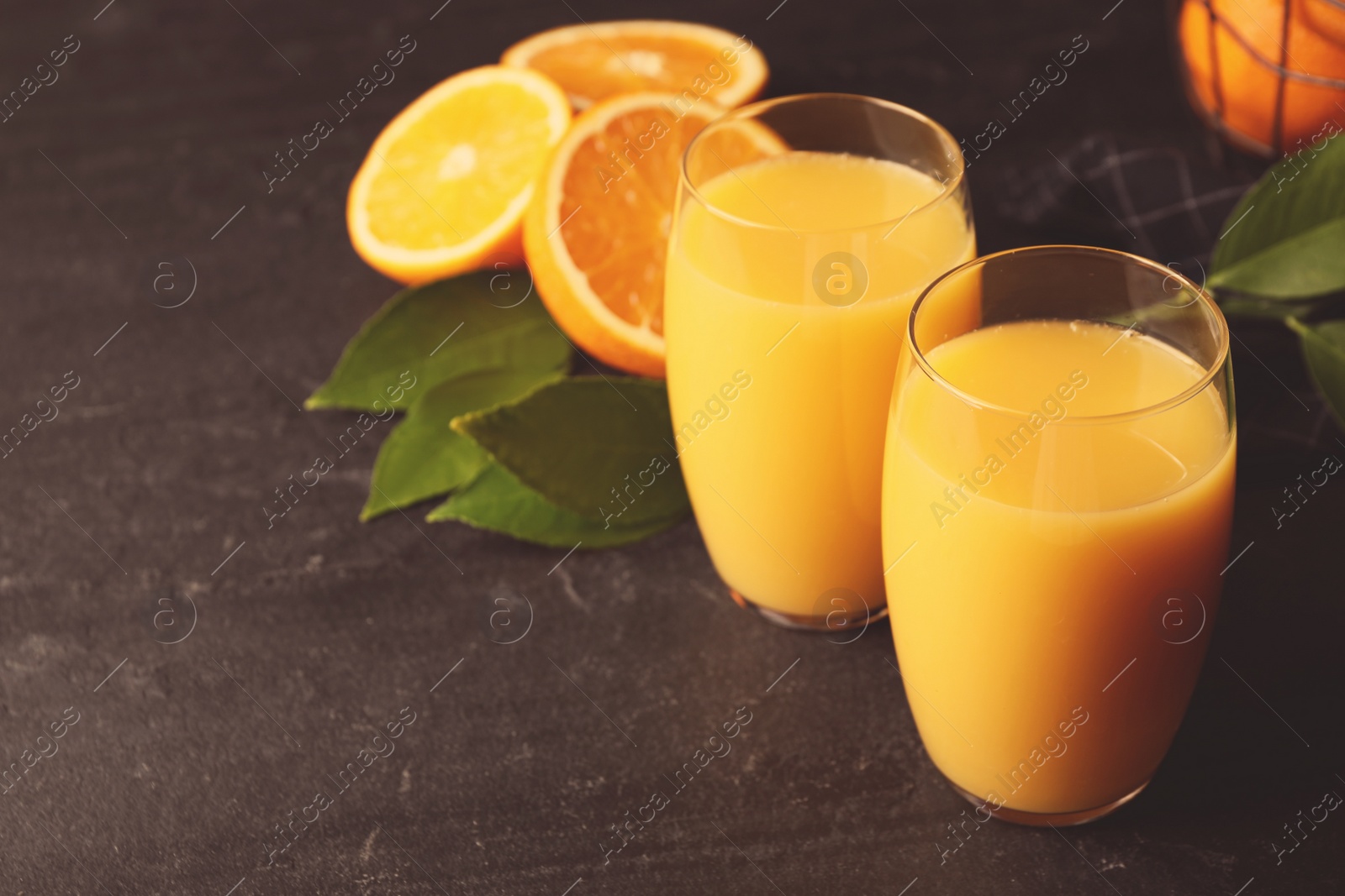 Photo of Glasses of orange juice and fresh fruits on black table. Space for text