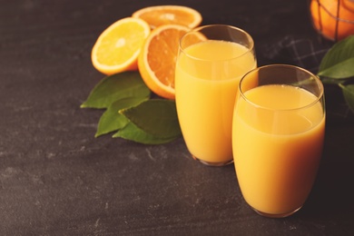 Photo of Glasses of orange juice and fresh fruits on black table. Space for text