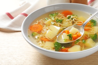 Photo of Spoon of fresh homemade vegetable soup over full bowl on wooden table, closeup