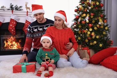 Photo of Happy family with Santa hats and Christmas gift in festively decorated room