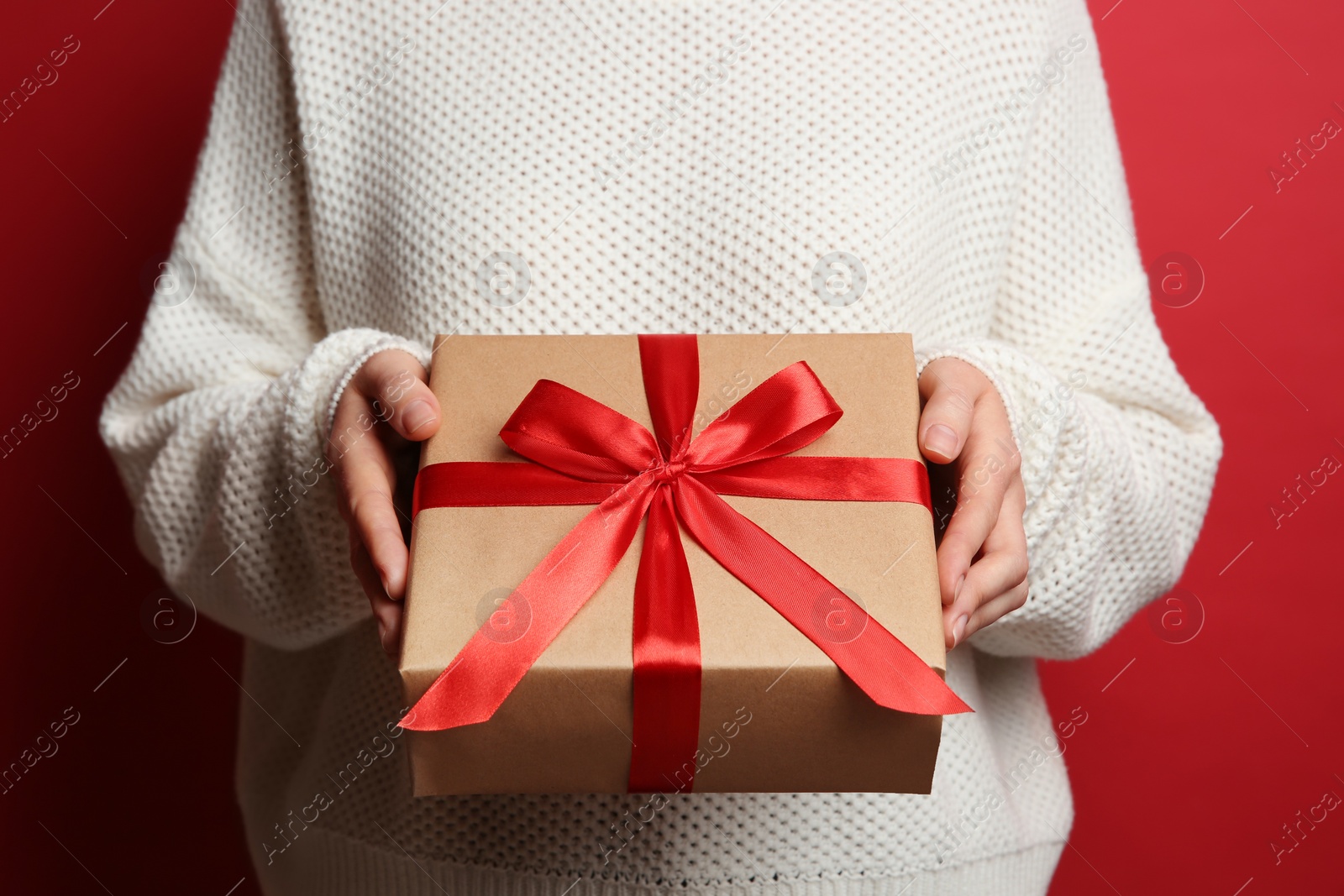 Photo of Woman holding Christmas gift box on red background, closeup