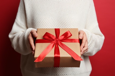 Woman holding Christmas gift box on red background, closeup