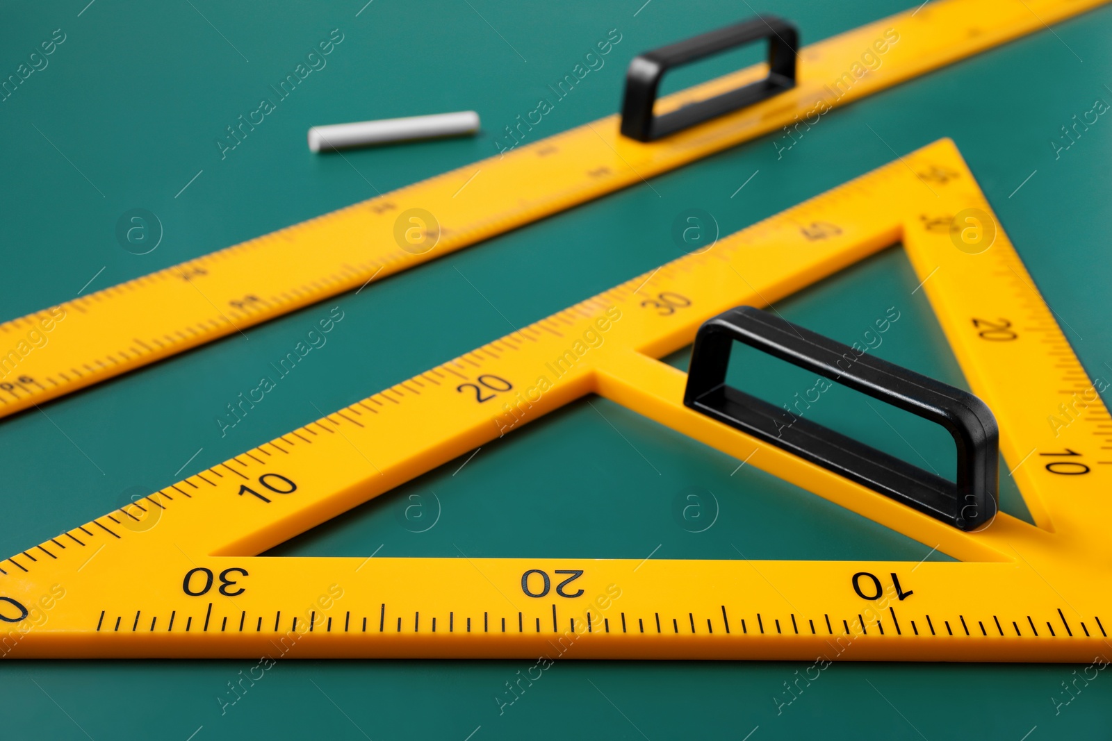 Photo of Triangle, ruler and chalk on green chalkboard, closeup