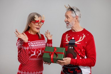 Photo of Couple in Christmas sweaters. Senior man presenting gift to his woman on grey background