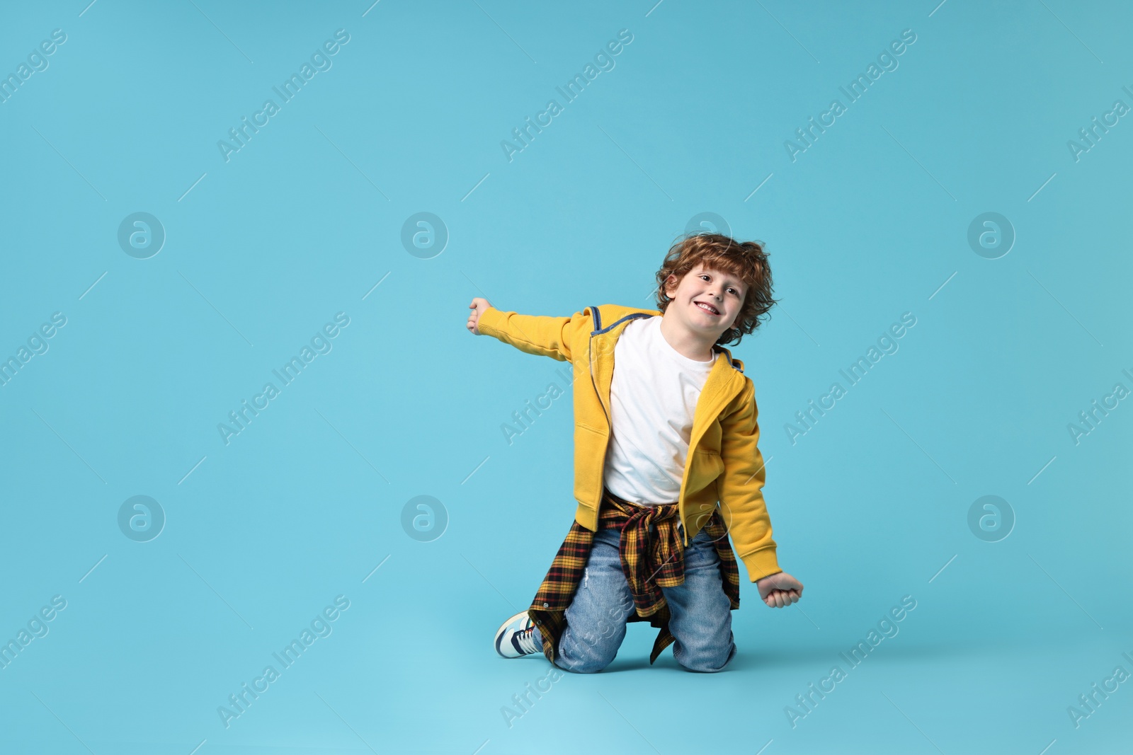 Photo of Happy little boy dancing on light blue background. Space for text