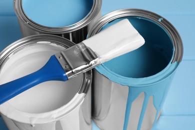 Photo of Cans of paints and brush on light blue background, closeup