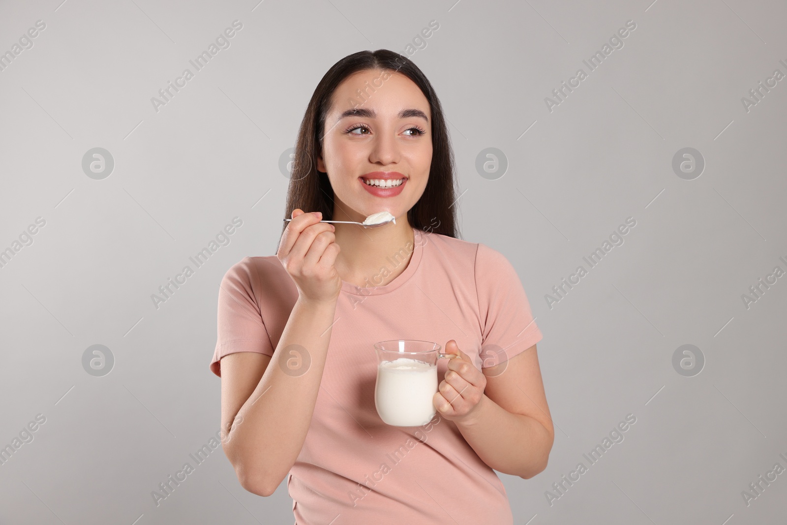 Photo of Happy woman eating tasty yogurt on grey background
