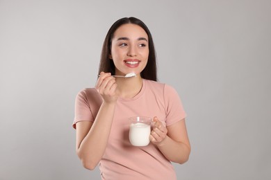 Photo of Happy woman eating tasty yogurt on grey background