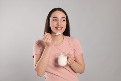 Happy woman eating tasty yogurt on grey background