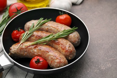 Photo of Frying pan with tasty homemade sausages, rosemary and tomatoes on brown textured table, closeup. Space for text