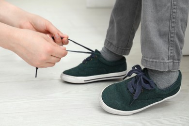 Mother helping son to tie shoe laces at home, closeup