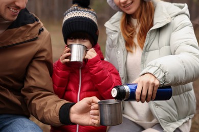 Photo of Happy family drinking hot tea together in forest, closeup
