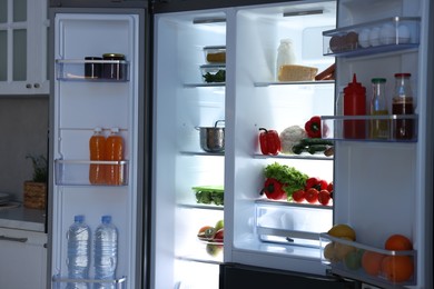 Open refrigerator full of different products in kitchen