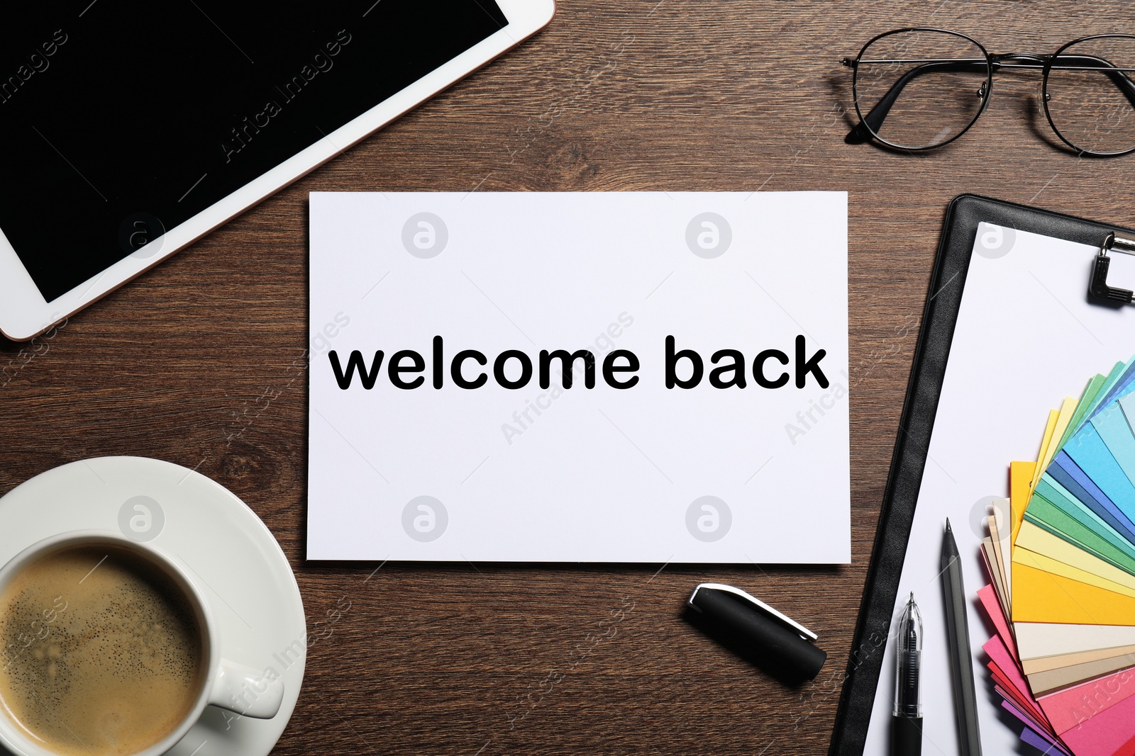 Image of Paper with phrase Welcome Back on wooden table. Office desk with tablet and coffee, flat lay