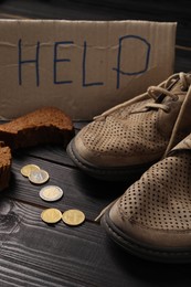 Photo of Poverty. Cardboard sign with word Help, old shoes, pieces of bread and coins on black wooden table