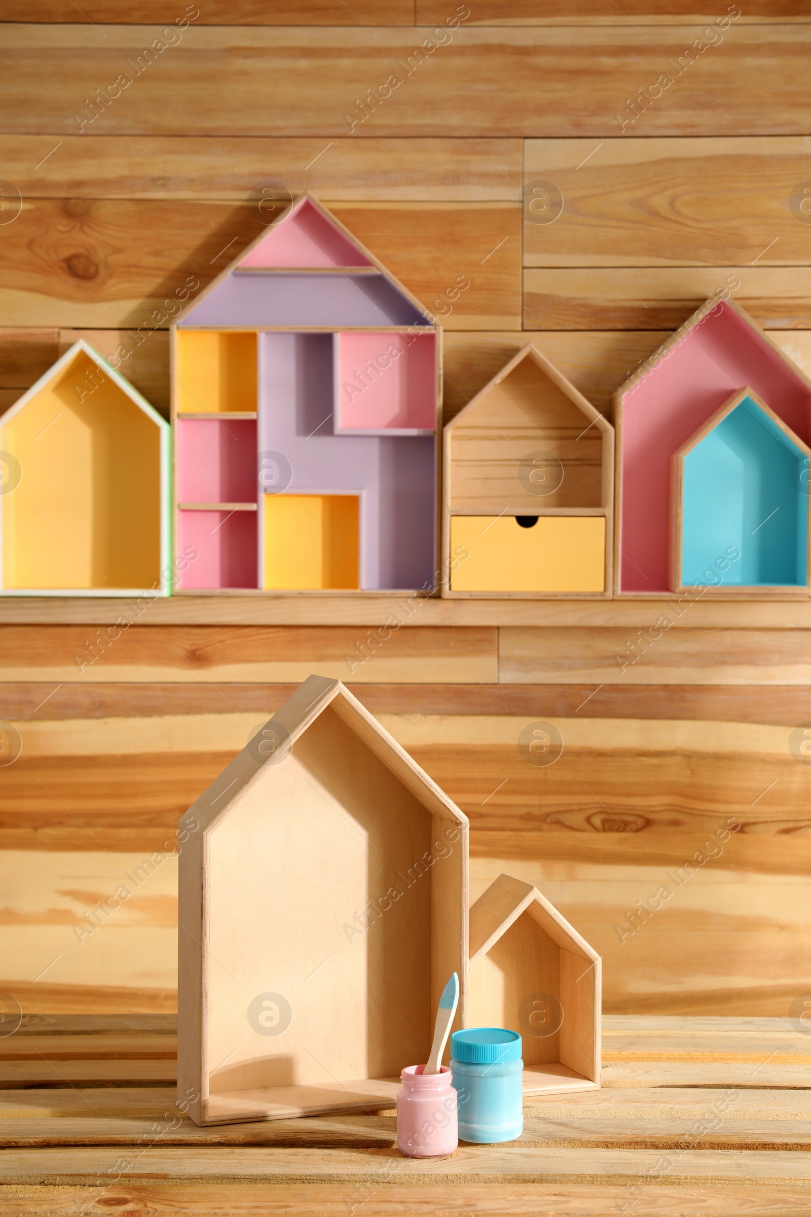 Photo of House shaped shelves, jars of paints and brush on wooden table. Interior elements