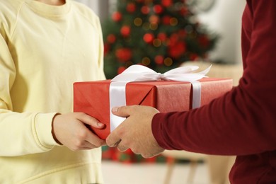 Photo of Man giving woman Christmas gift box indoors, closeup. Sending present by mail