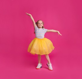 Photo of Cute little girl in tutu skirt dancing on pink background
