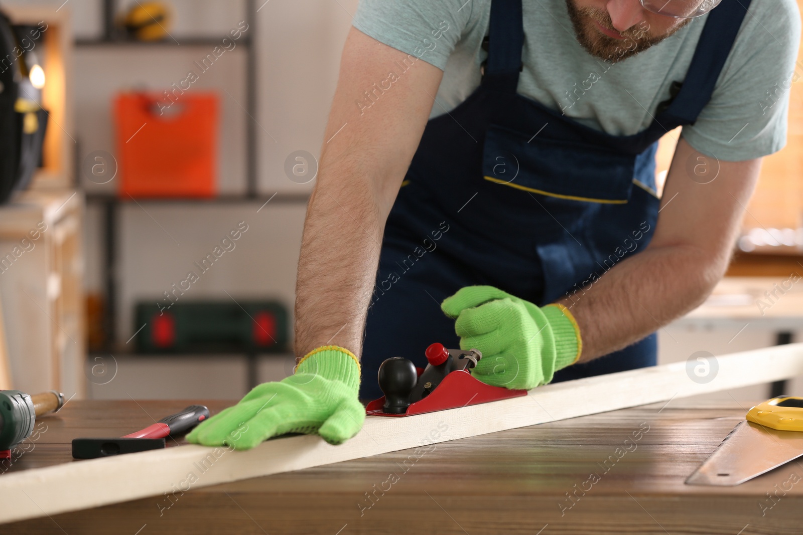 Photo of Carpenter shaping wooden bar with hand plane at table in workshop, closeup