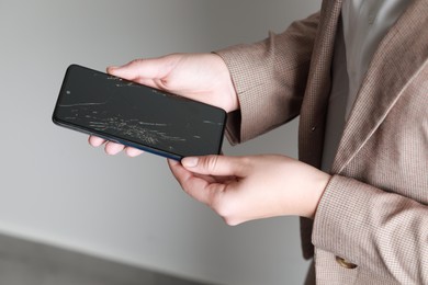 Photo of Woman holding damaged smartphone near light grey wall, closeup. Device repairing