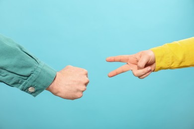 People playing rock, paper and scissors on light blue background, closeup