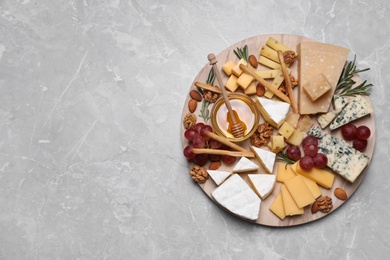 Cheese plate with honey, grapes and nuts on light grey marble table, top view. Space for text