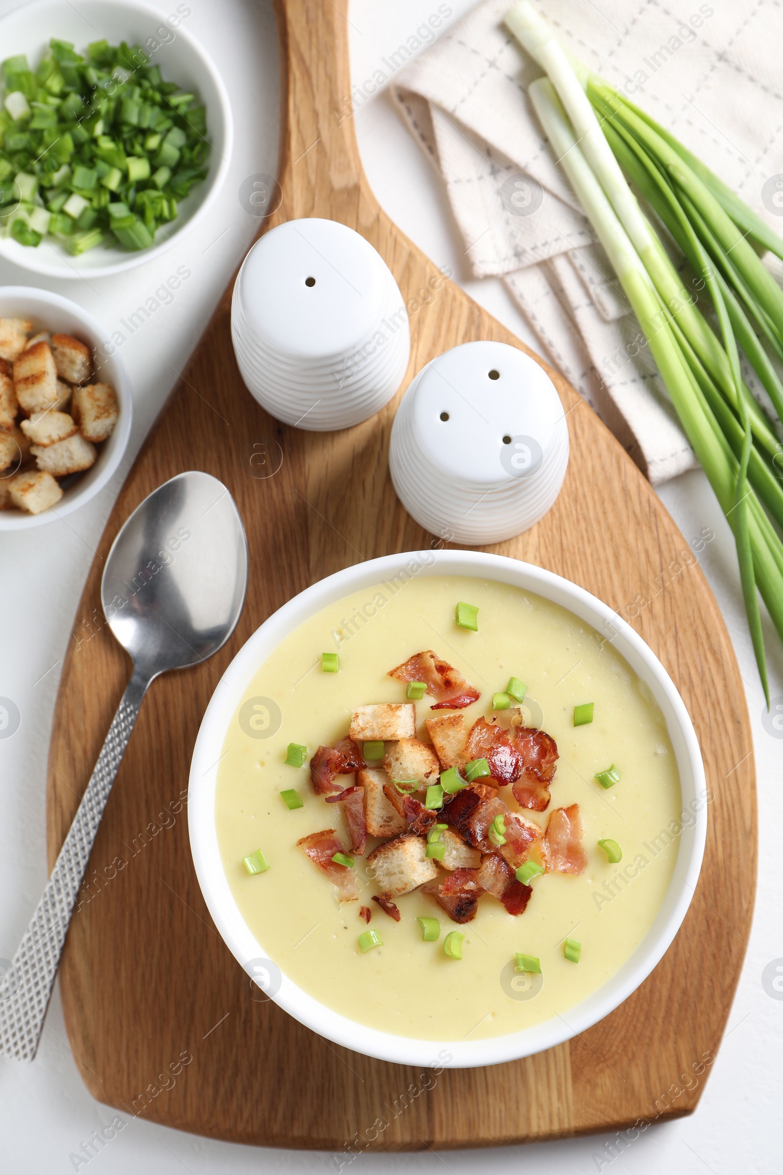 Photo of Tasty potato soup with bacon in bowl served on white table, flat lay