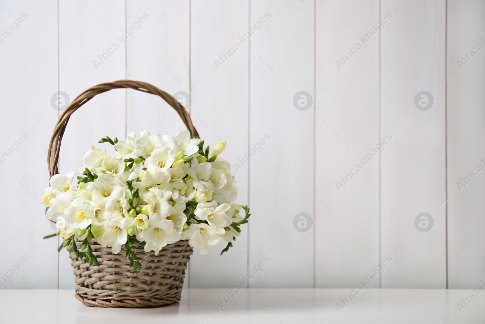 Photo of Beautiful freesia flowers in basket on white table. Space for text