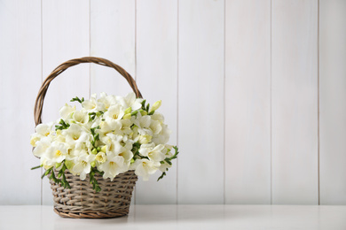 Beautiful freesia flowers in basket on white table. Space for text