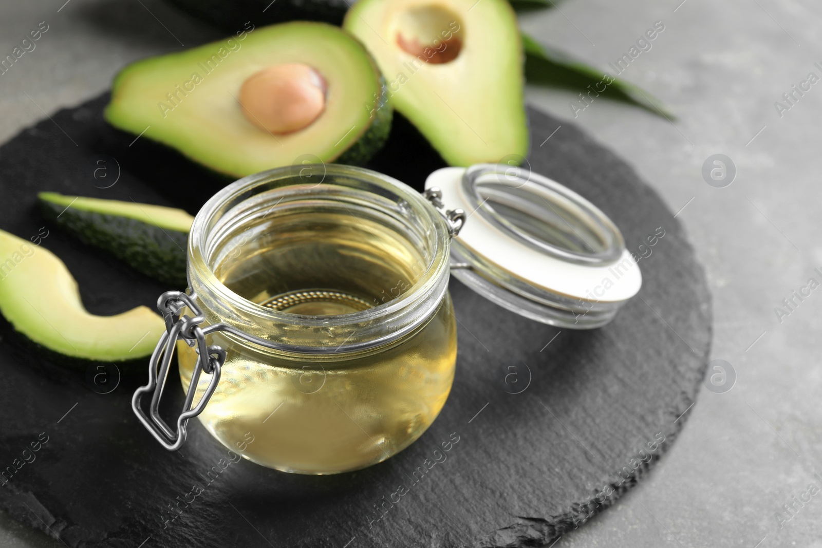 Photo of Board with jar of natural oil and avocados on grey stone background. Space for text