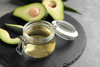 Board with jar of natural oil and avocados on grey stone background. Space for text