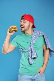 Handsome man eating tasty burger on color background