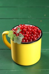 Photo of Ripe red currants and leaves in mug on green wooden table. Space for text