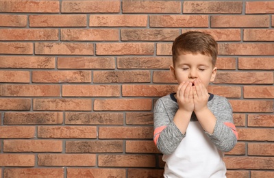 Cute boy suffering from cough near brick wall. Space for text