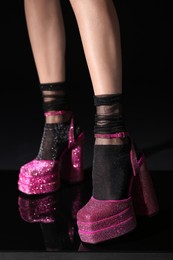 Photo of Woman wearing pink high heeled shoes with platform and square toes on black background, closeup