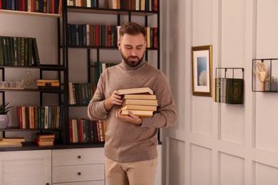 Photo of Young man with stack of different books in home library