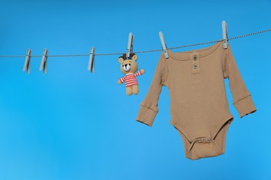 Photo of Baby onesie and bear toy drying on laundry line against light blue background, space for text