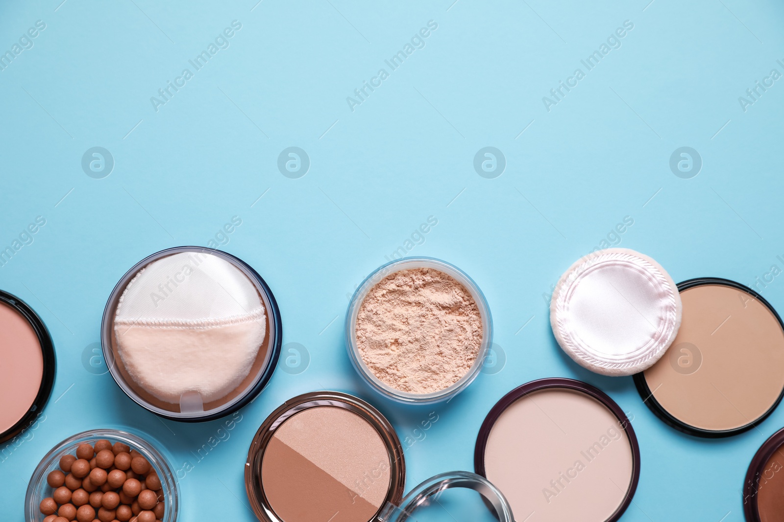 Photo of Different face powders on light blue background, flat lay. Space for text