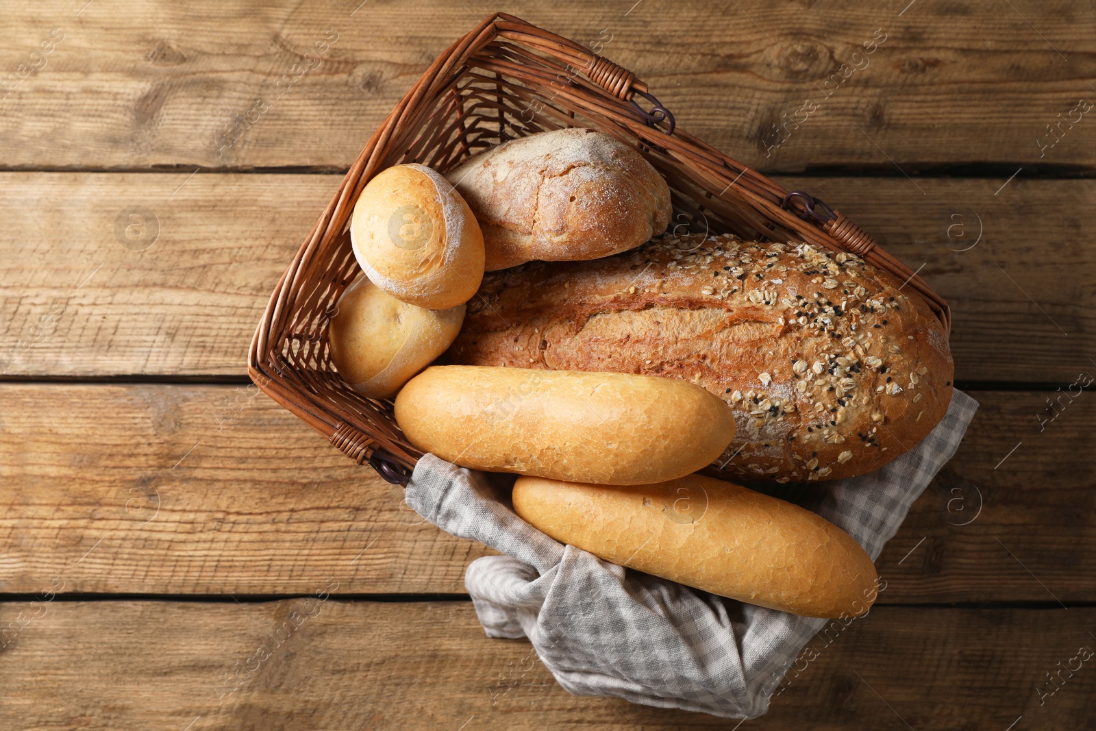 Photo of Wicker basket with different types of bread on wooden table, top view