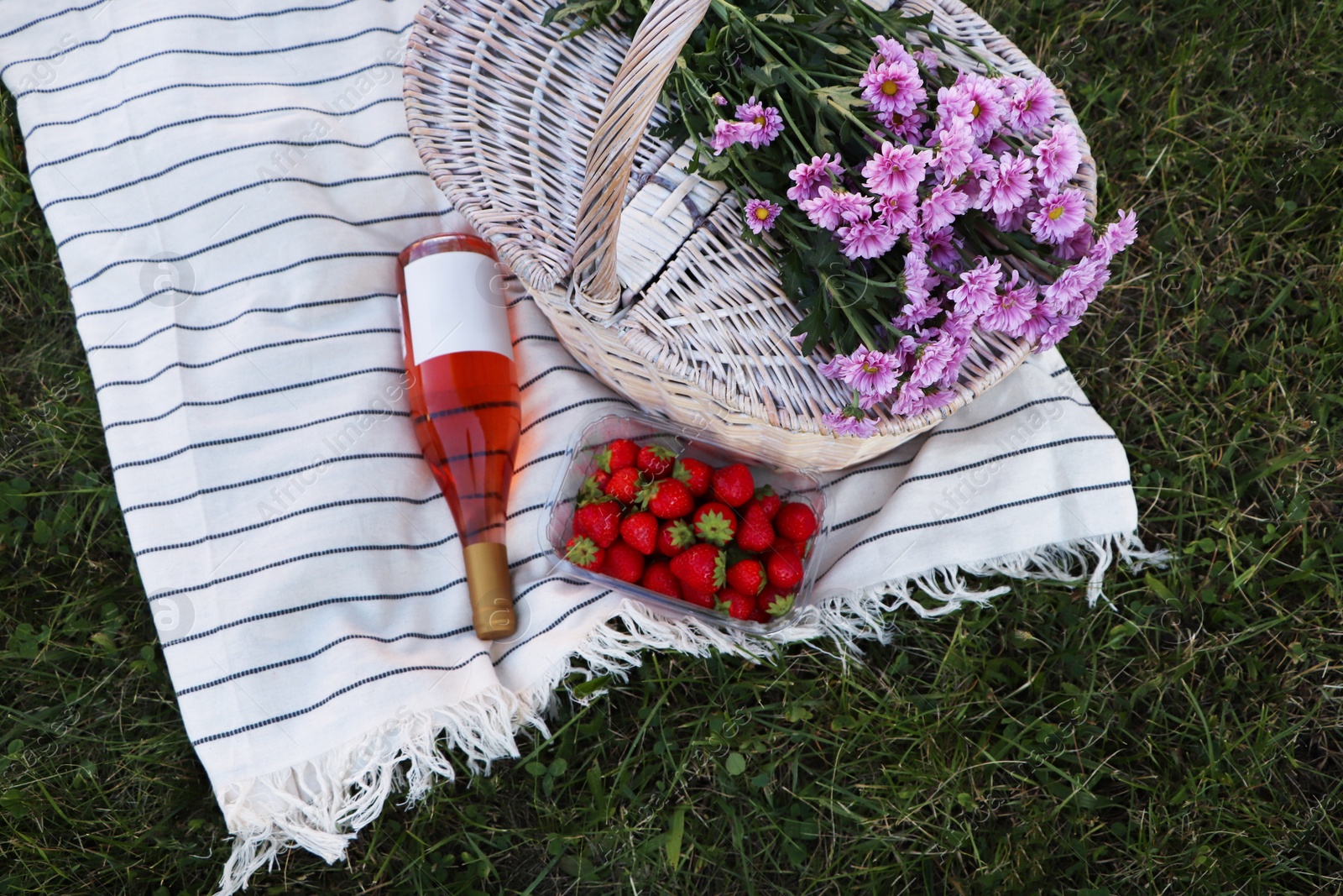 Photo of Picnic basket, flowers, bottle of wine and strawberries on blanket outdoors