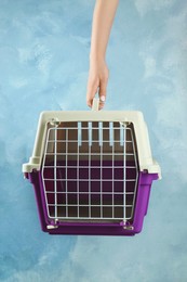 Photo of Woman holding violet pet carrier against light blue wall, closeup