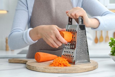Photo of Woman grating fresh ripe carrot at kitchen table, closeup