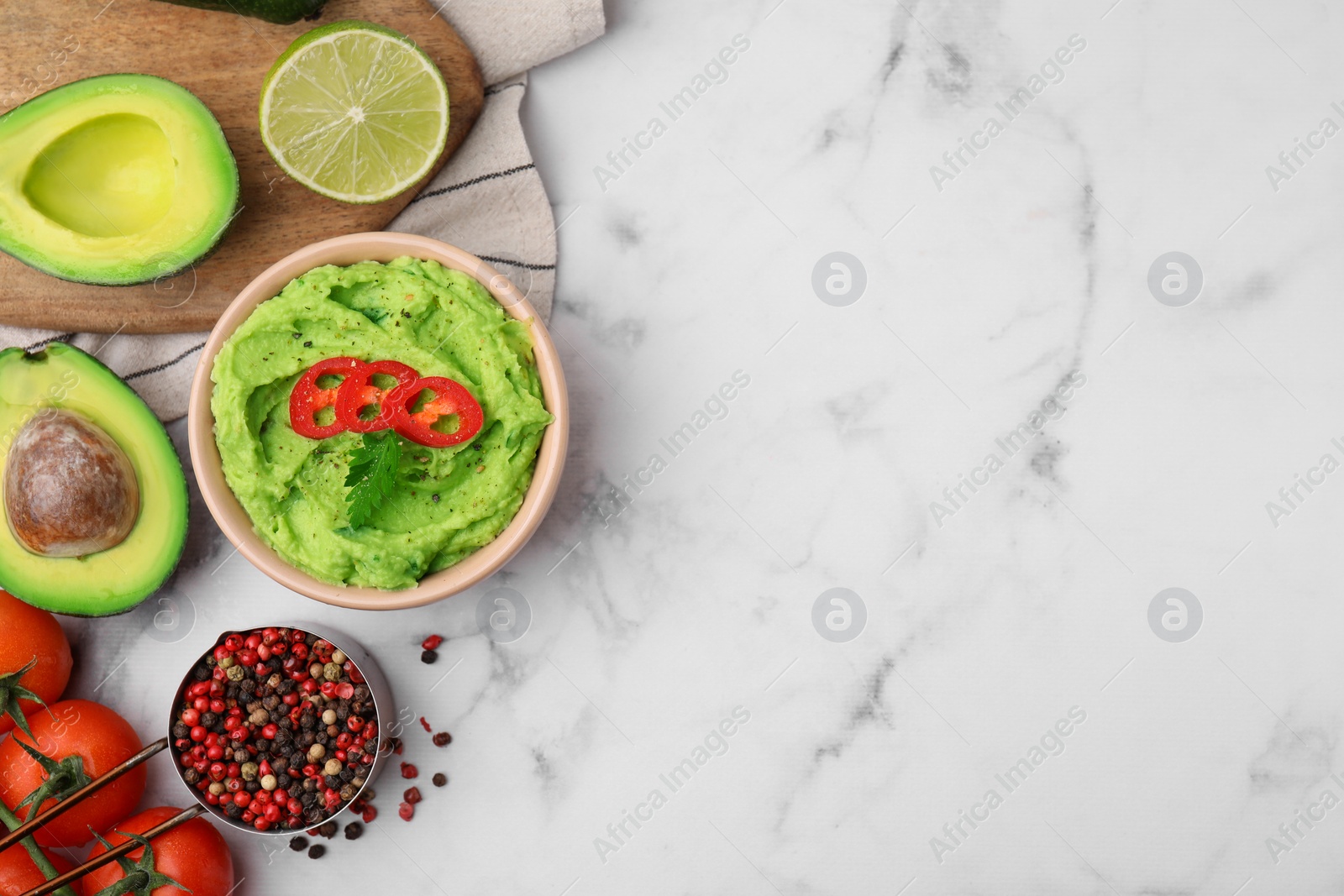 Photo of Bowl of delicious guacamole and ingredients on white marble table, flat lay. Space for text