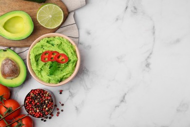 Photo of Bowl of delicious guacamole and ingredients on white marble table, flat lay. Space for text